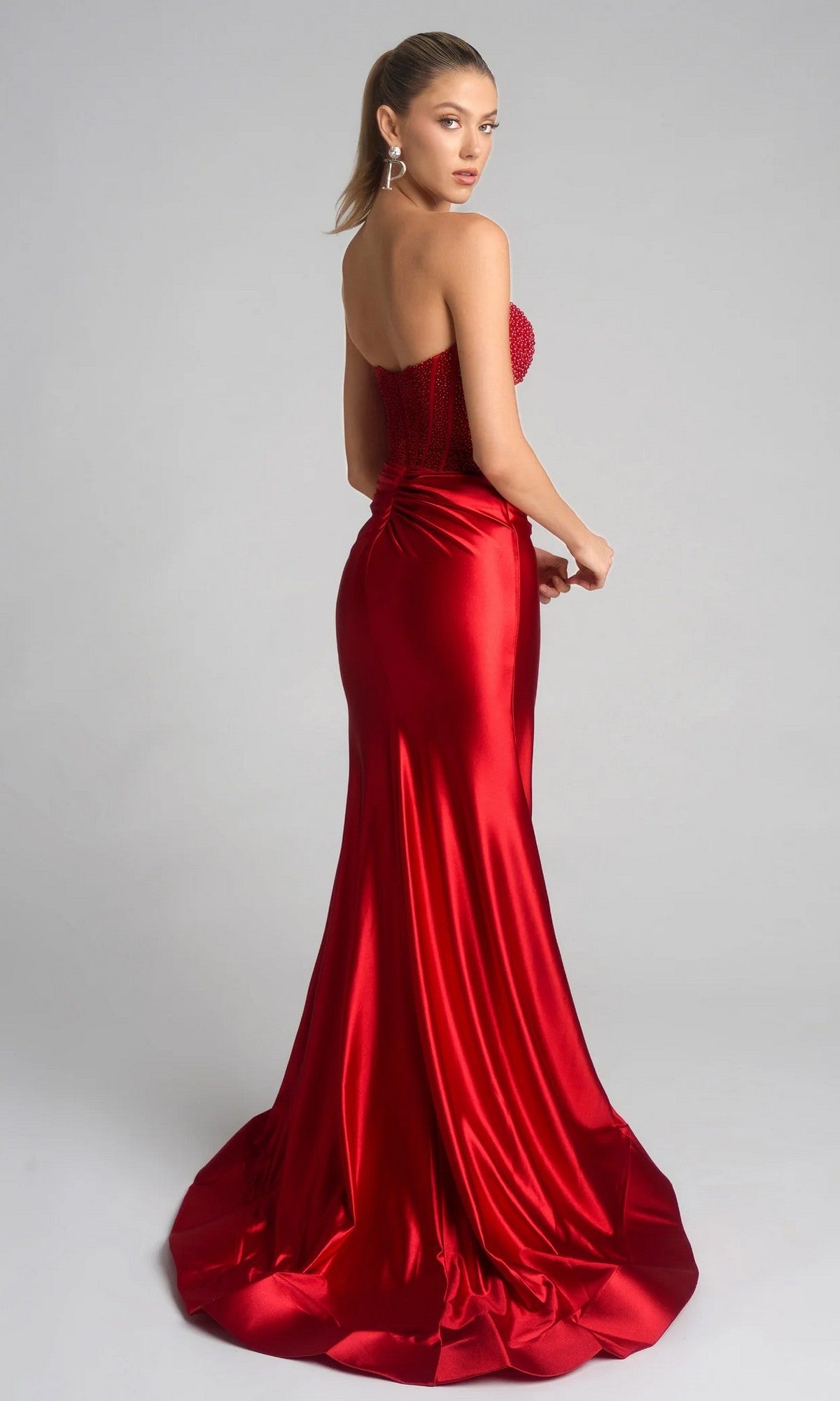 A woman in the Portia and Scarlett PS26039 long prom dress, with a beaded corset bodice and flared train, stands against a plain light background.
